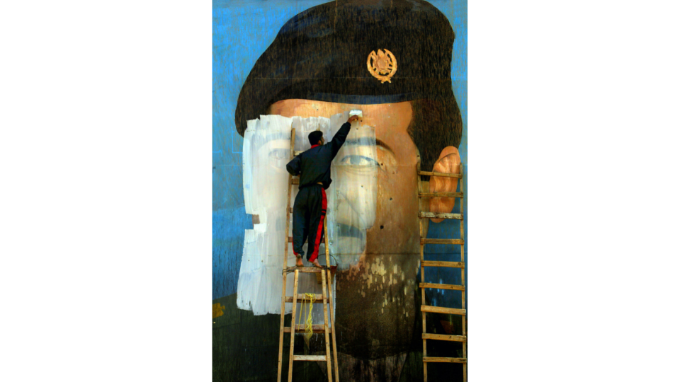 Une photo de Saddam Hussein, criblée d’impacts de balles, est recouverte de peinture par Salem Yuel, Bagdad, Irak, avril 2003, Photo Carolyn Cole